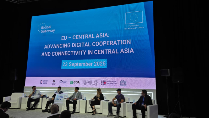 Konferences paneļdiskusija ar pieciem runātājiem uz skatuves, fonā liels ekrāns ar pasākuma nosaukumu “EU - Central Asia: Advancing Digital Cooperation and Connectivity in Central Asia” un datumu “2025. gada 23. septembris”. Pasākums notiek Eiropas Savienības finansētās iniciatīvas “Global Gateway” ietvaros. Ekrāna apakšā redzami dažādu organizāciju logotipi